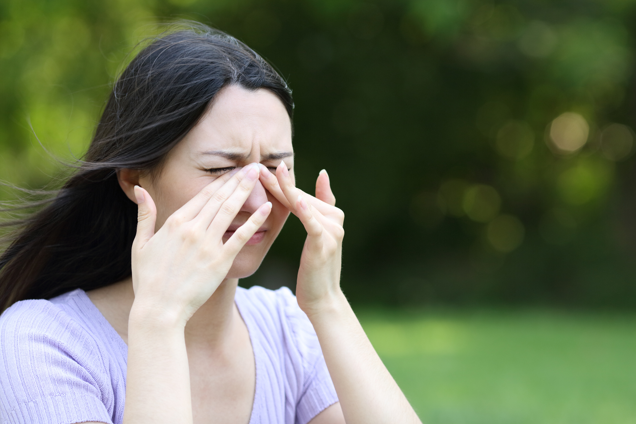 Woman experiencing sinus pressure outdoors.